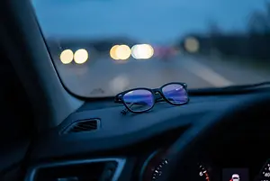 Eyeglasses resting on a car dashboard at night with blurred headlights outside