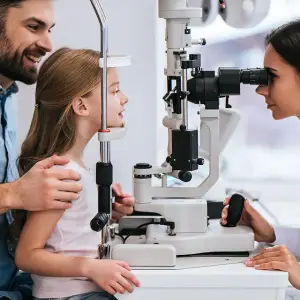 A young girl with her parents at an optometrist's office getting an eye exam.