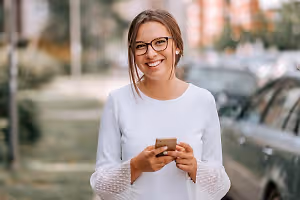 A woman wearing eyeglasses is standing and smiling on the side of the road.