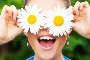 Woman holding two white daisies with yellow centers in front of her face