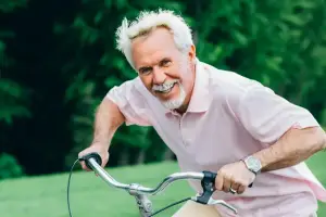 An older man riding a bicycle on a sunny day in a park