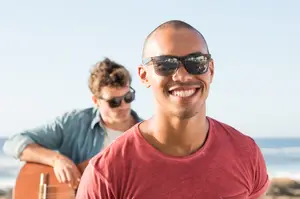 Two men are smiling and posing for a photo, one playing guitar and the other standing next to him