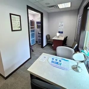 A room that has a desk, chairs, a mirror, and a poster on the wall