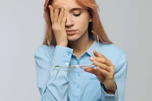 woman holding glasses and covering her forehead with her hand