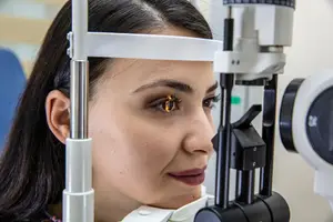 A woman with long hair is looking into an eye exam machine, she is smiling.