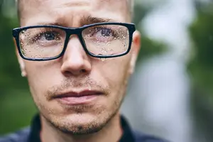 A man wearing glasses with raindrops on the lens and water drops on his face
