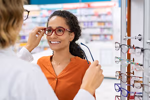 A woman trying on glasses with the help of another woman inside a store