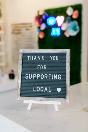 A sign on a marble counter reads 'Thank You For Supporting Local' in white letters against a green background.