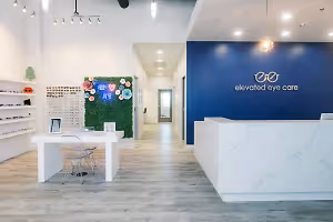 Interior of an eye care office with white and blue decor and a desk with a monitor and glasses on display.