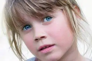 Close-up of a young girl with blonde hair and blue eyes looking directly at the camera