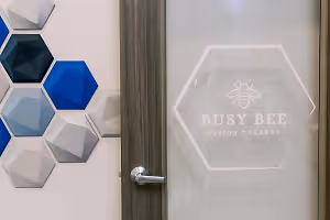 A glass door with a white hexagonal sign displaying Busy Bee Vision Therapy and a blue and gray hexagonal wall design