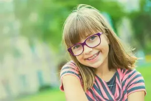 A girl wearing glasses is smiling and posing for a photo in a park