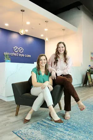 Two women sitting on a couch in an eye care clinic lobby smiling for the camera