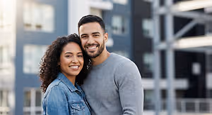 A man and woman smiling at the camera outside of an apartment building.