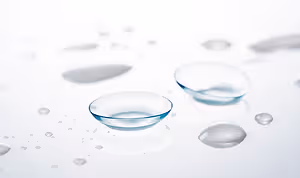 Close up of two contact lenses sitting on a white surface with water droplets around them.