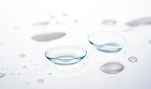 Close up of two contact lenses sitting on a white surface with water droplets around them.