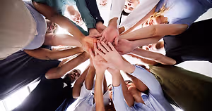 A group of people gathered in a circle, with their hands placed on top of each other in the center
