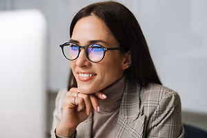 A woman wearing glasses is smiling while looking at something in front of her.