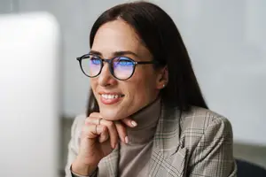 A woman wearing glasses is smiling while looking at something in front of her.
