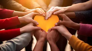 Group of people with different colored shirts holding a heart shaped paper cutout