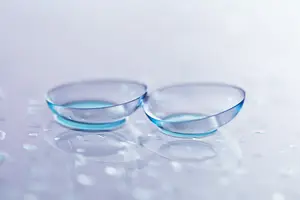 Two transparent contact lenses sitting on a shiny surface with water droplets around them