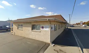 A building with the address 321 2nd St So, located in Nampa, Idaho, has signage on its side and a parking lot in front, with cars parked and a road with traffic behind it.