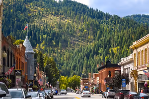 A street in a town surrounded by mountains and green trees on a sunny day