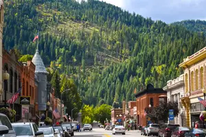 A street in a town surrounded by mountains and green trees on a sunny day