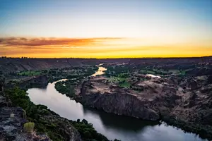 A wide landscape view of a river flowing through a canyon with a sunset in the background.