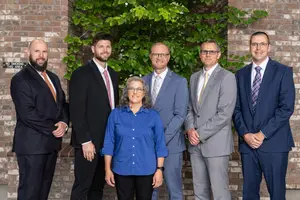 Five people dressed in suits and glasses standing in front of a brick wall with a plant behind them