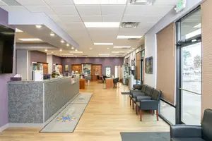 Reception area of a clinic with a counter, chairs, and a television mounted on the wall.
