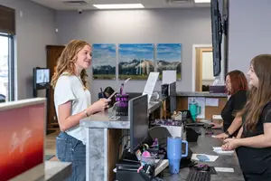 Four women in a room working at a counter with computers and a monitor in the background