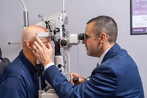 An adult male is getting his eyes checked by an optometrist at an eye clinic