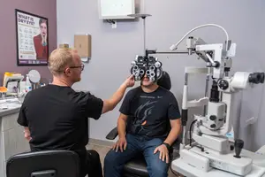 An adult man is helping a young man put on an eye test machine