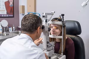 A woman is having her eyes examined by a man in a white coat using a machine.