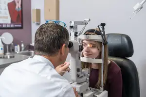 A woman is having her eyes examined by a man in a white coat using a machine.