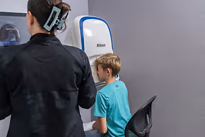 A young boy is having his eyes examined by an eye doctor using a Nikon device.