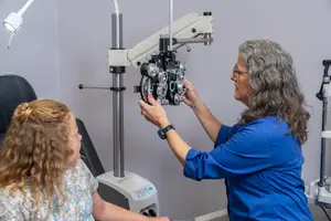 An optometrist adjusting a phoropter on a young girl's eye.