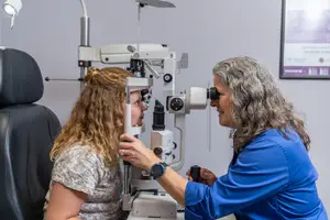 An optometrist is examining a young woman's eyes using a slit lamp.