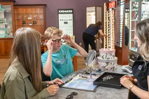 A boy tries on glasses at an optical store with a woman and a man behind the counter