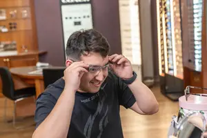 A man is adjusting his glasses while smiling and holding his forehead