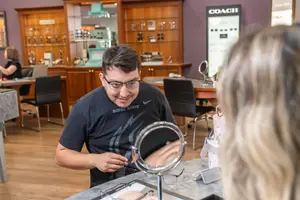 A man in glasses is helping a woman try on glasses in an eyeglass store