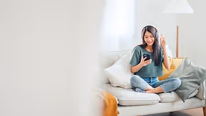 A woman sitting on a couch wearing headphones and holding a cell phone with a smile on her face