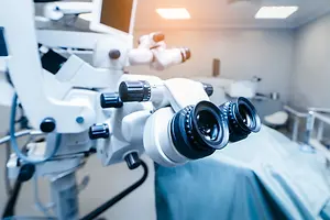 An operating microscope with a monitor in an operating room with a blue cloth on the bed
