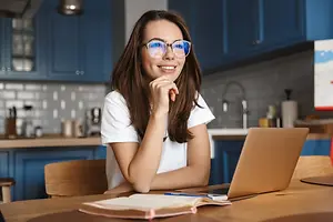 Woman sitting at a table in a kitchen with a laptop and books