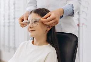 A woman is getting her glasses adjusted by a doctor in a white coat in a room with glass frames on display