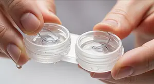 A person is holding two clear glass containers with a contact lens in each one