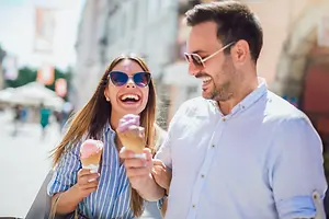 A man and woman smiling and laughing together while holding ice cream cones on a city street