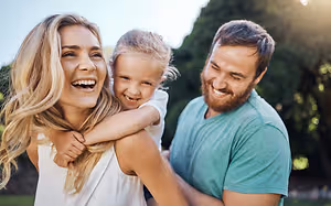 A family with a woman and two children smiling and standing in an outdoor area
