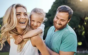 A family with a woman and two children smiling and standing in an outdoor area